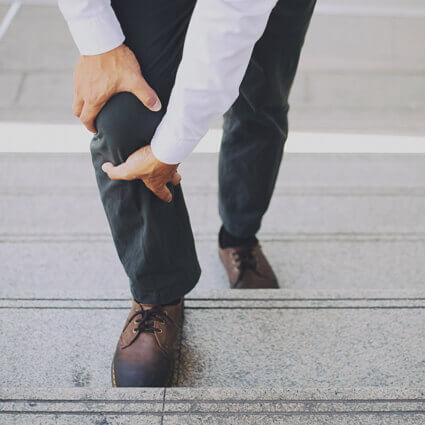 business-man-walking-up-stairs-holding-leg-in-pain-sq (1)